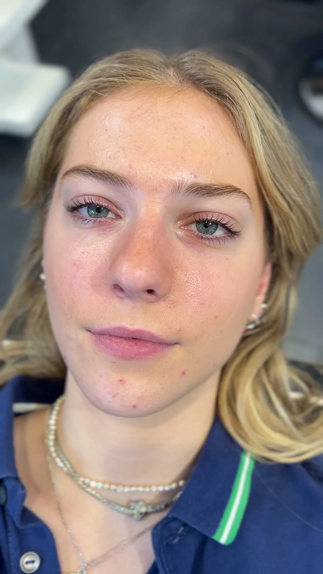 Client seated in the salon with natural lifted lashes and shaped brows, salon interior behind her