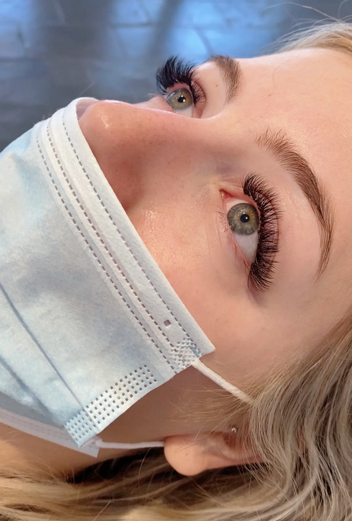 Side profile of a client — a long curled lash extension set in sharp relief against the light