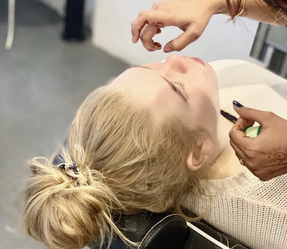 Therapist holding cotton thread taut over a client's brow during eyebrow threading