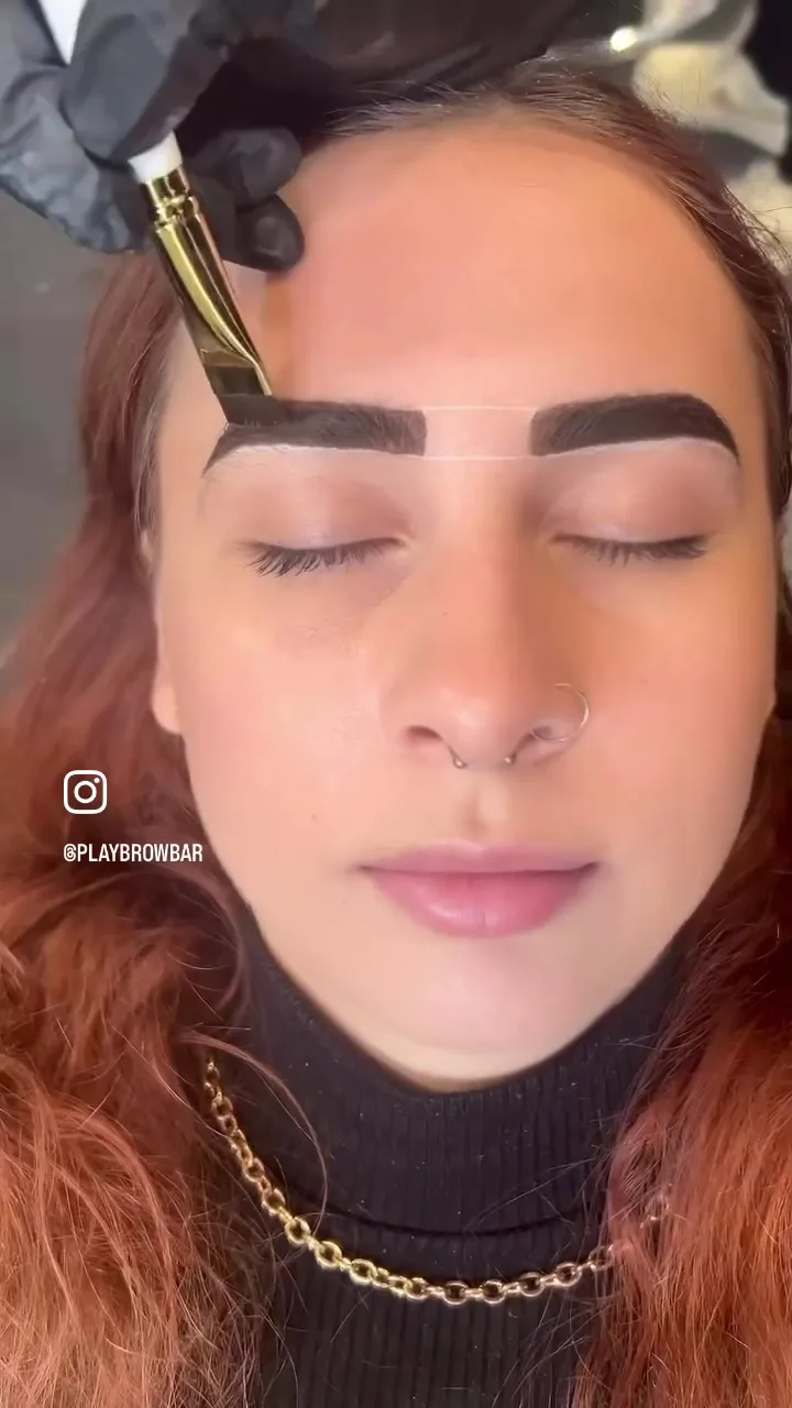 Henna brow tint being painted on with a gold angled brush