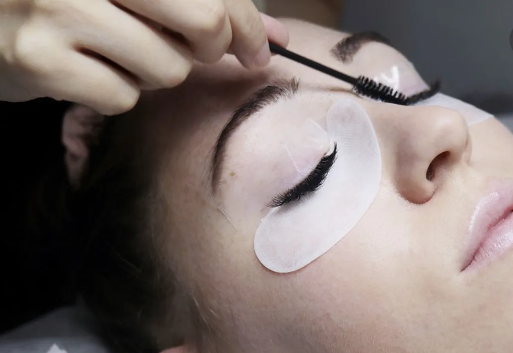 Lash treatment in progress — technician brushing a client's lashes with lash pads fitted under both eyes